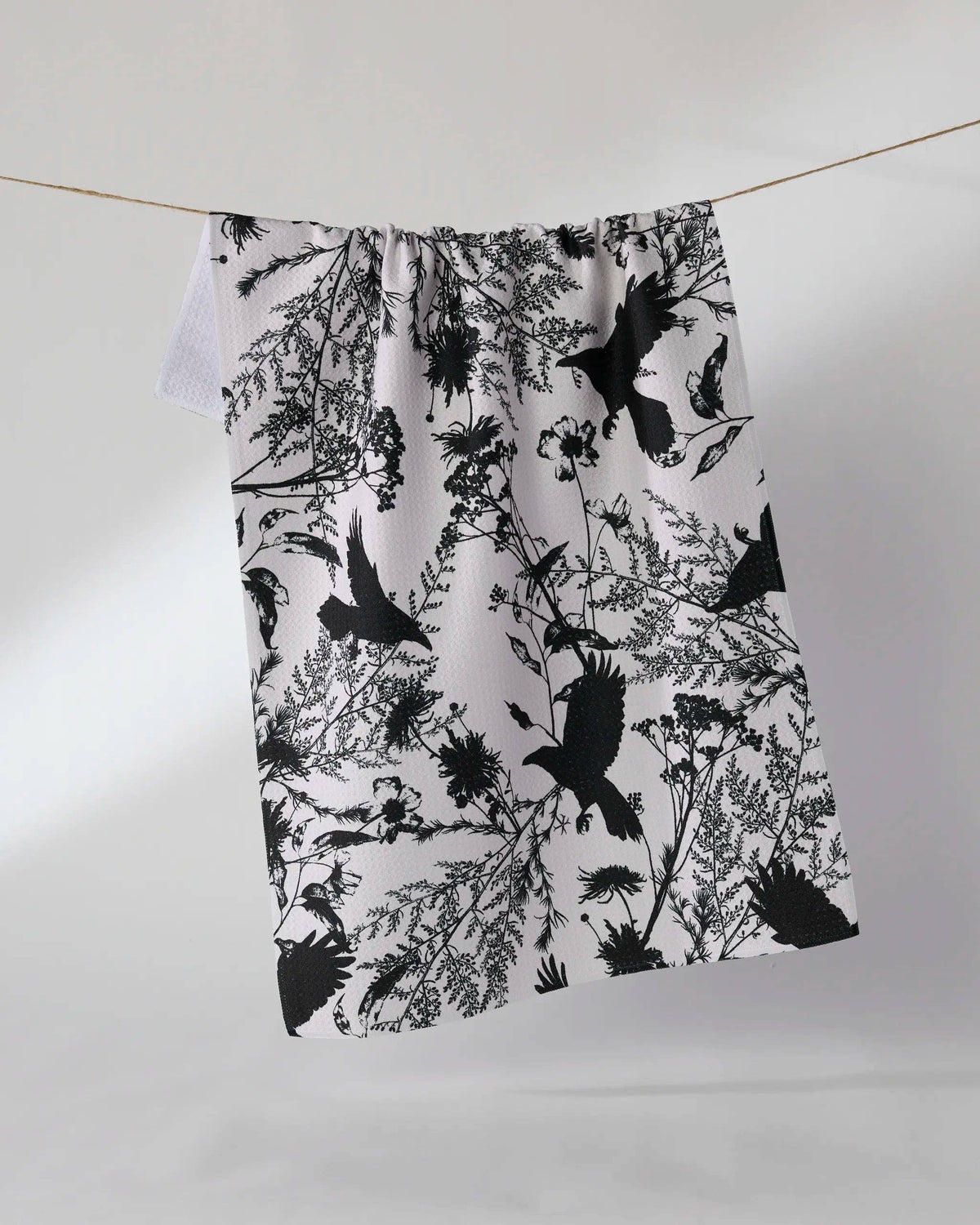 Spooky printed tea towel with crows and fall foliage on a white background.