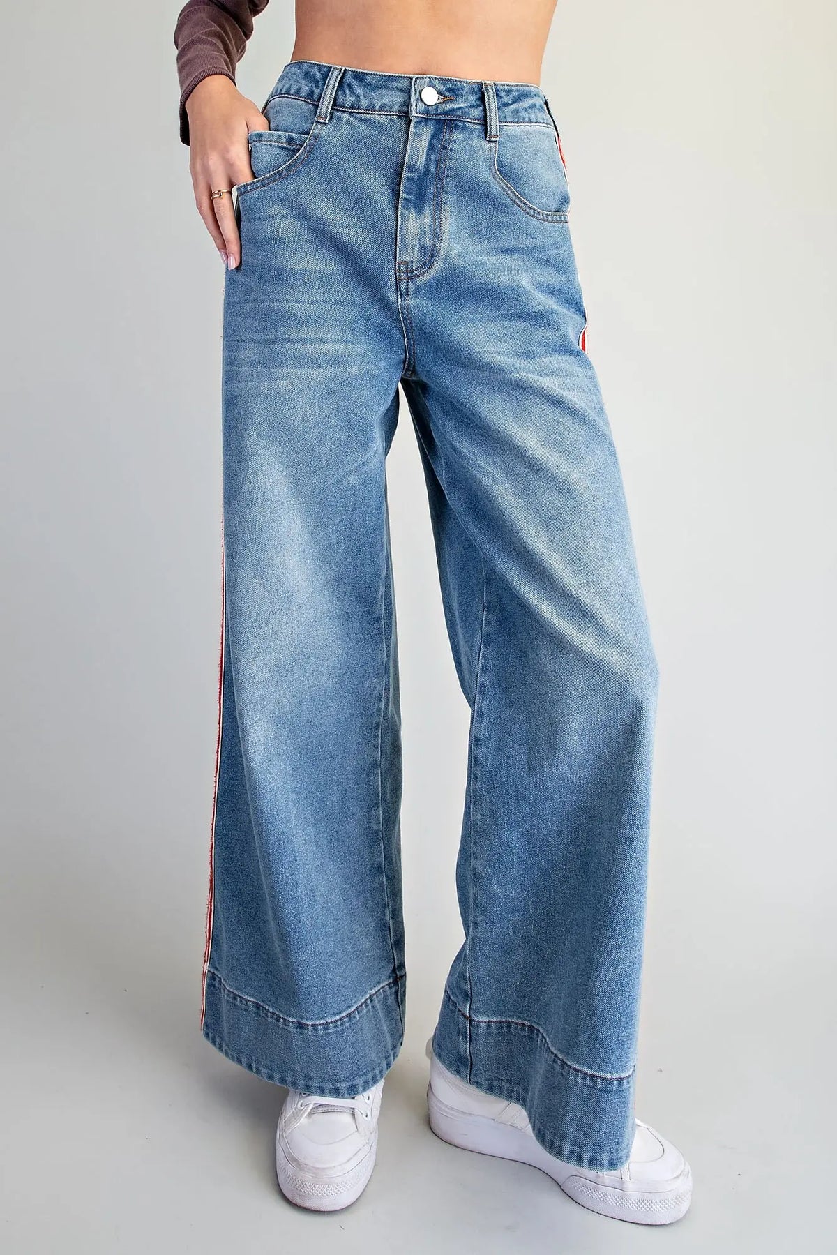 A person wearing high-waisted, wide-leg blue denim jeans with white sneakers, shown from the waist down against a plain light gray studio background.