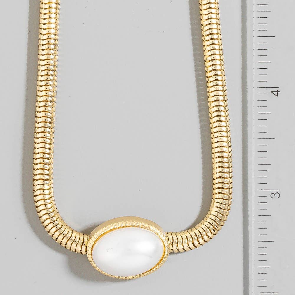 Gold necklace with a white pendant on a gray background with a ruler for scale.