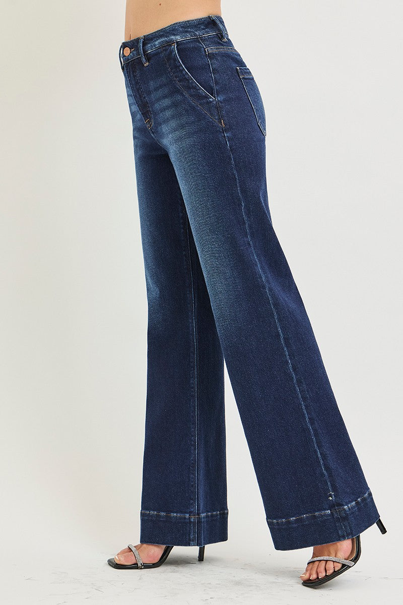 A person wearing dark blue wide-leg denim jeans with a cuffed hem and black strappy high-heeled sandals, shown from the waist down against a plain light background.