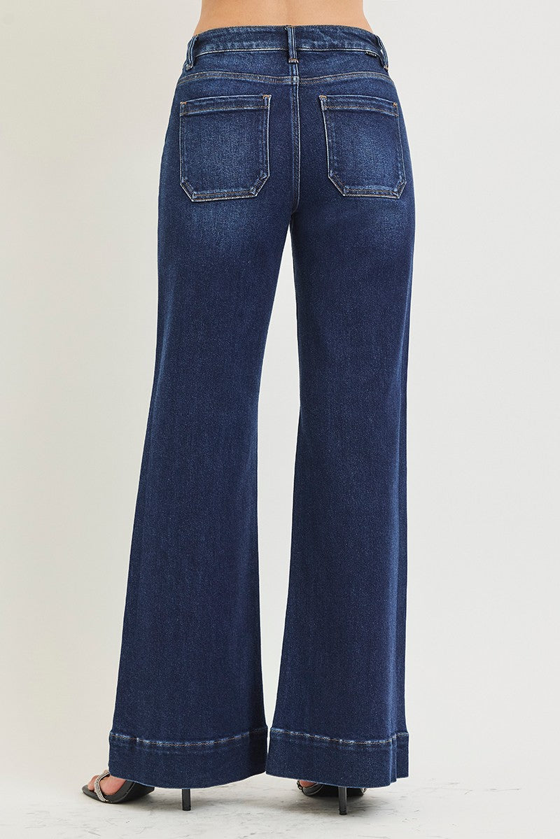 A person wearing dark blue wide-leg denim jeans with a cuffed hem and black slide sandals, shown from the waist down against a plain light background.