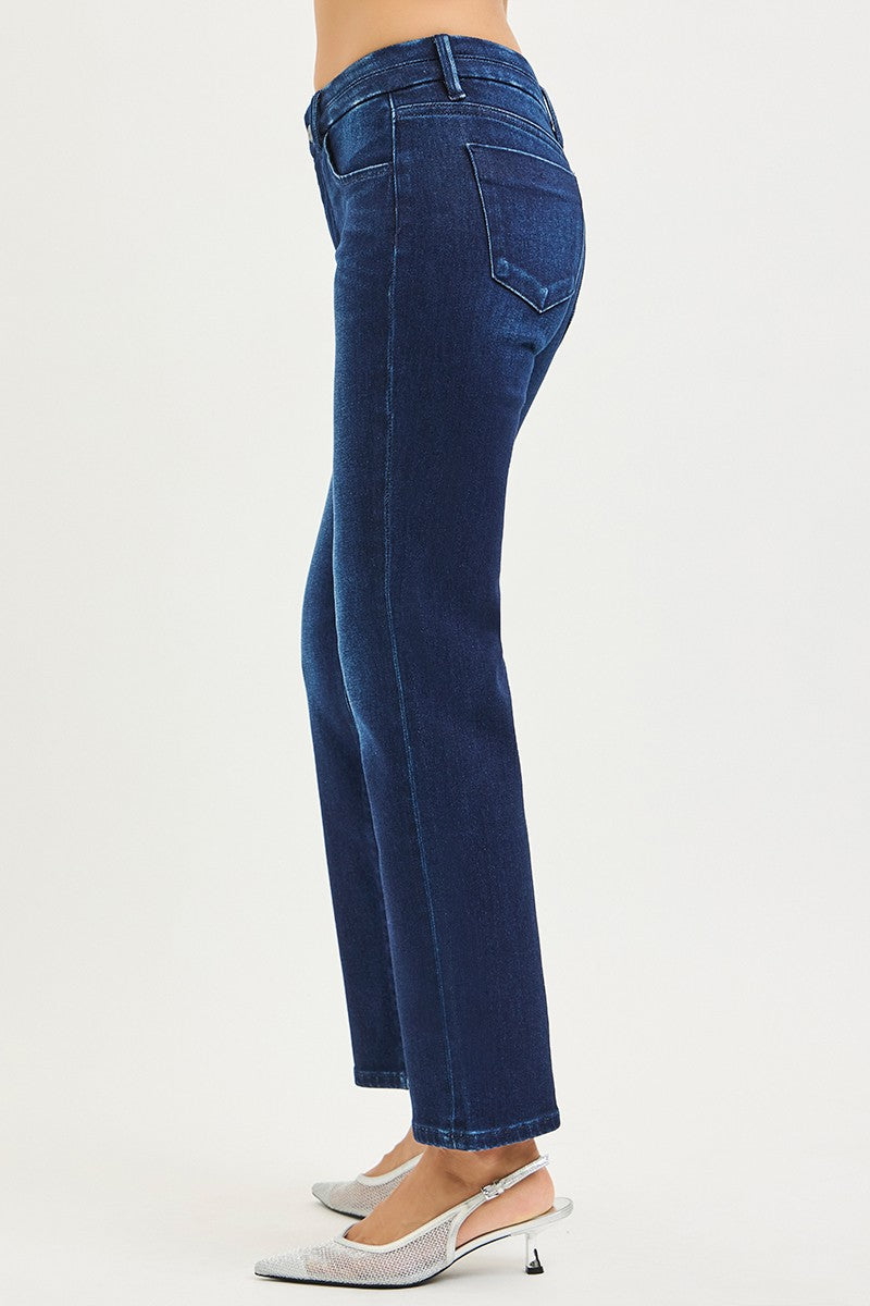 A side profile view of a person wearing dark blue straight-leg jeans and white slingback heels against a plain white studio background.