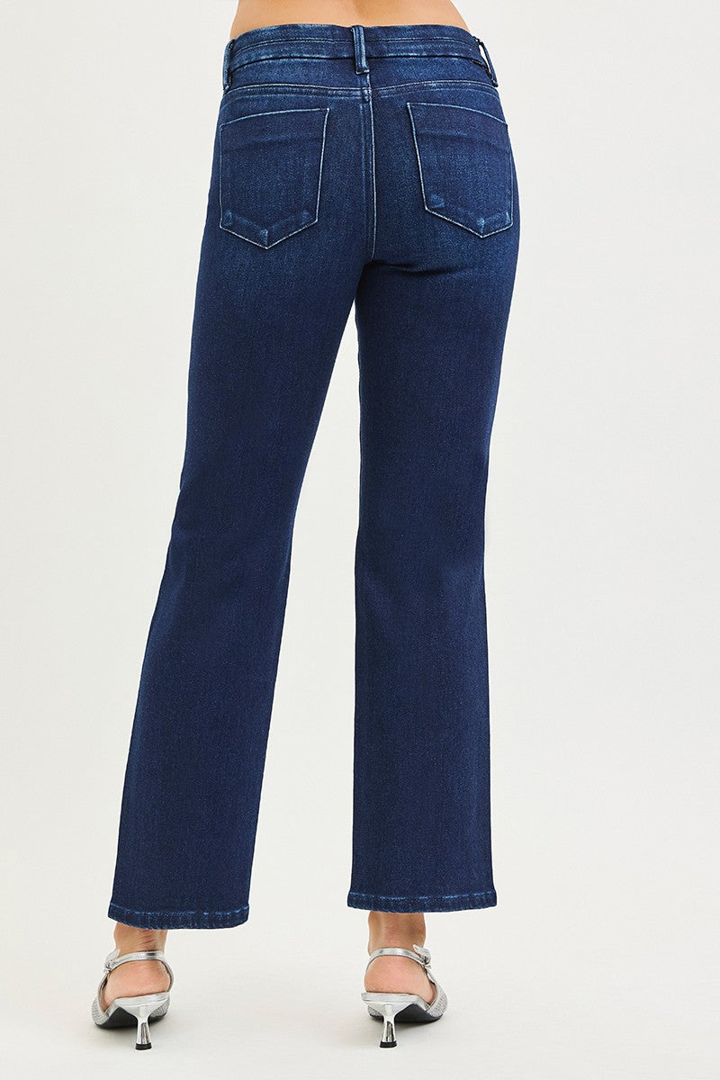 Rear view of a person wearing dark blue denim flare jeans with silver high-heeled sandals, shown against a plain light gray studio background.