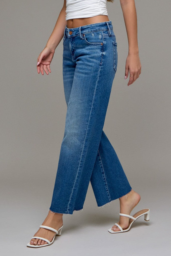 Woman wearing a white top and cropped classic straight blue jeans on a gray background