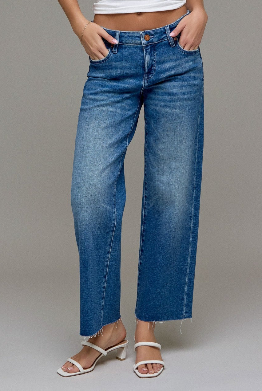 Woman wearing a white tank top and cropped classic straight blue jeans against a plain background