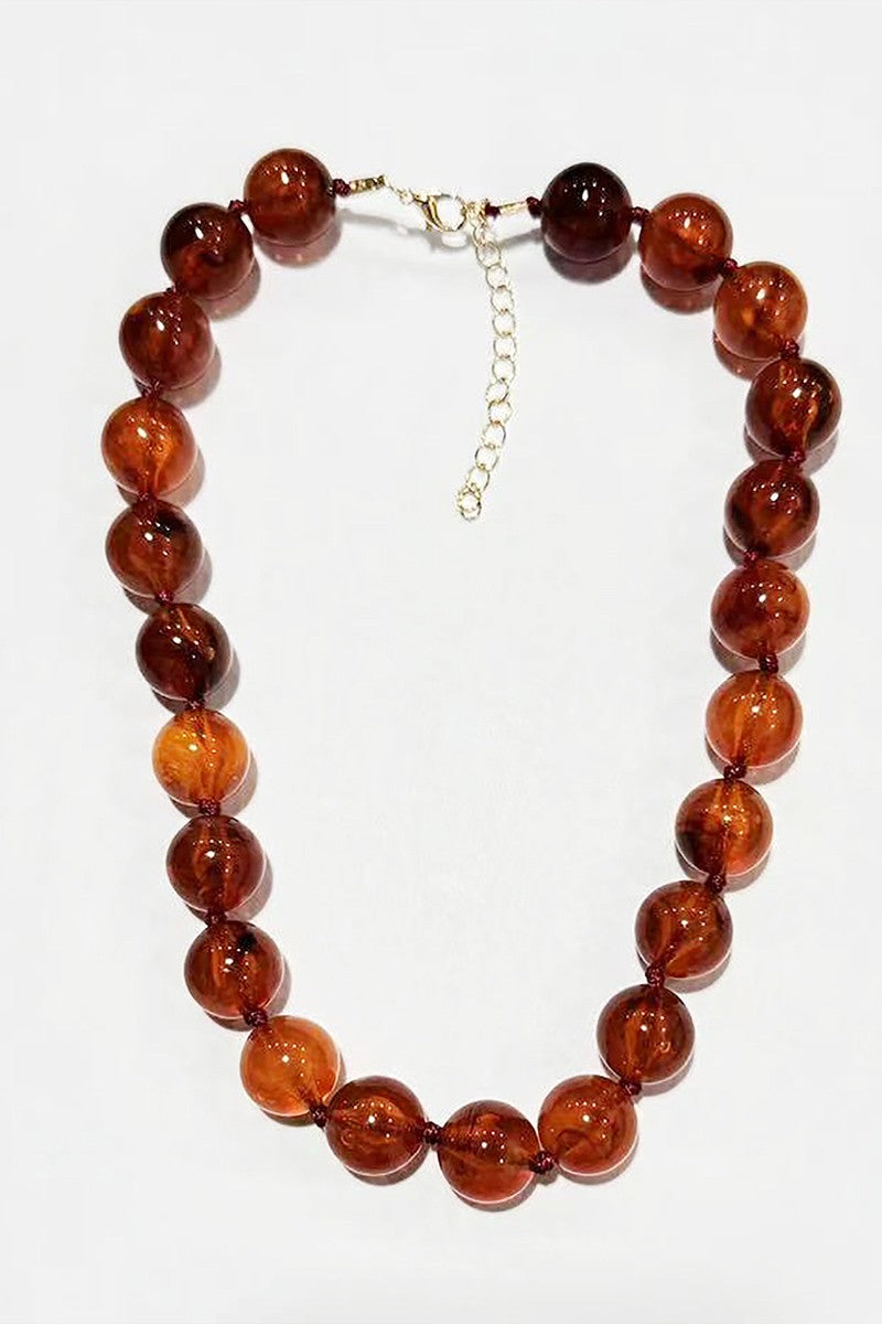 A beaded necklace made of polished round amber-brown glass beads with a small silver chain extender and clasp, shown on a plain white background.
