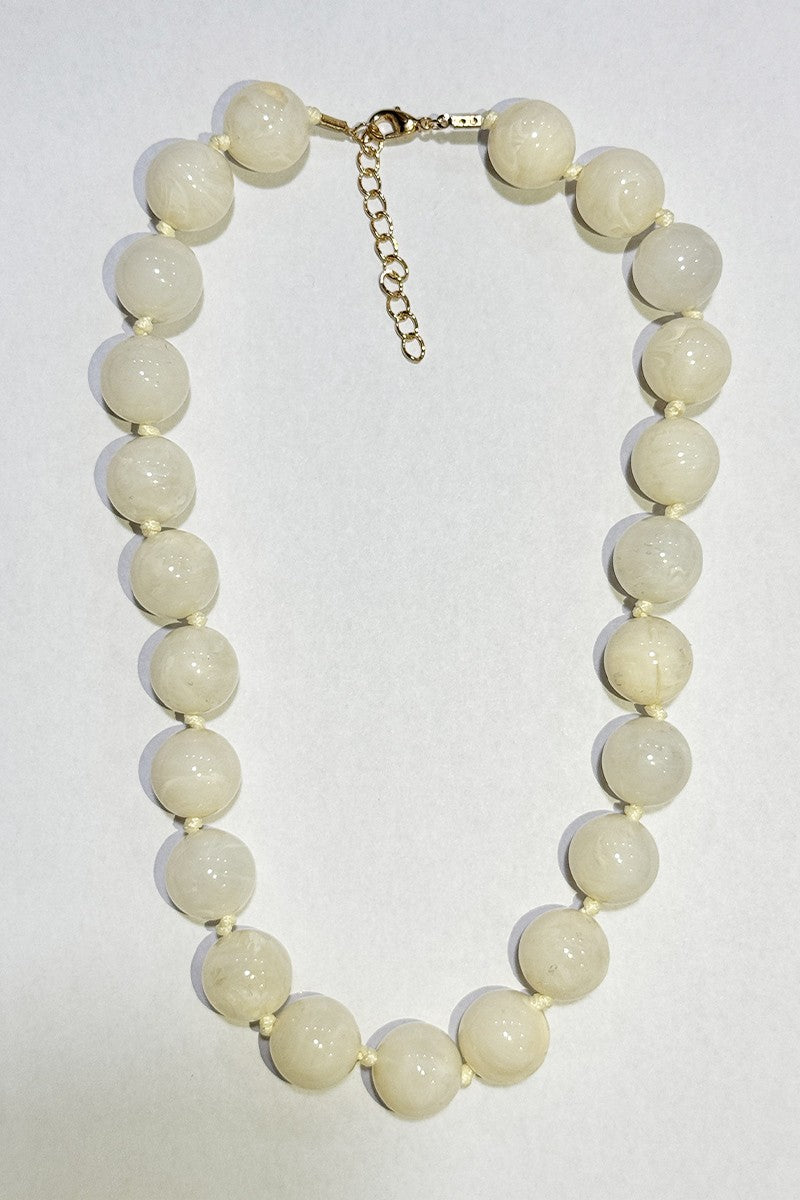 A beaded necklace made of large, round, glossy ivory beads with a gold-tone clasp and extender chain, displayed on a plain light background.