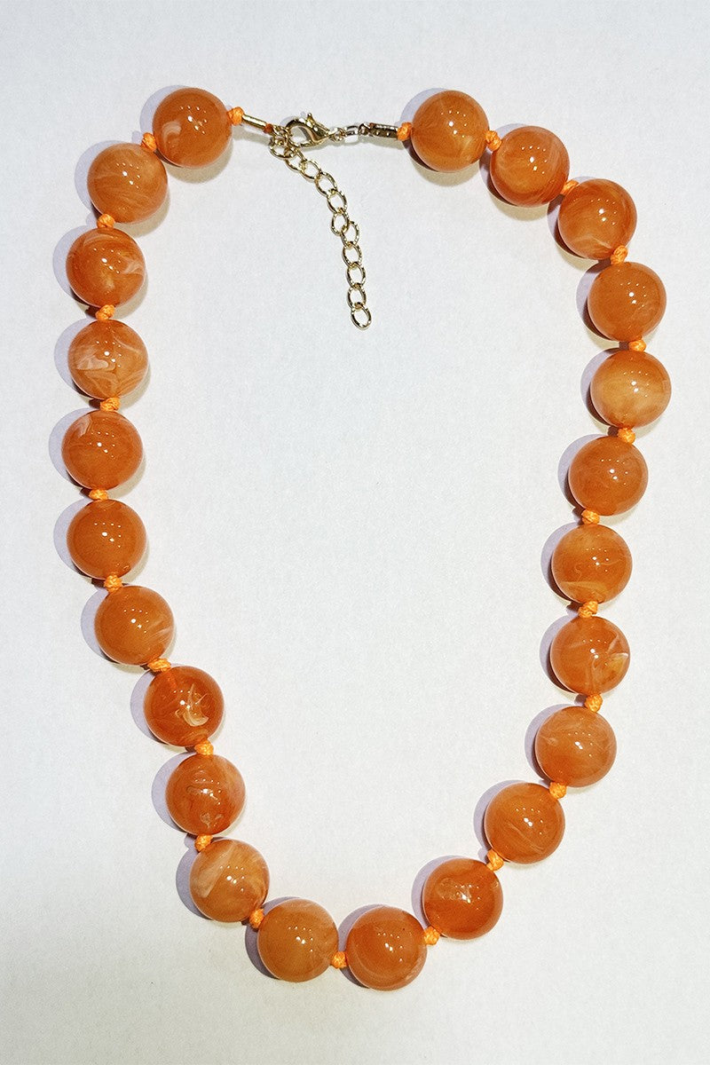 A beaded necklace made of polished orange beads with a small gold-tone clasp and extension chain, photographed on a plain white background.
