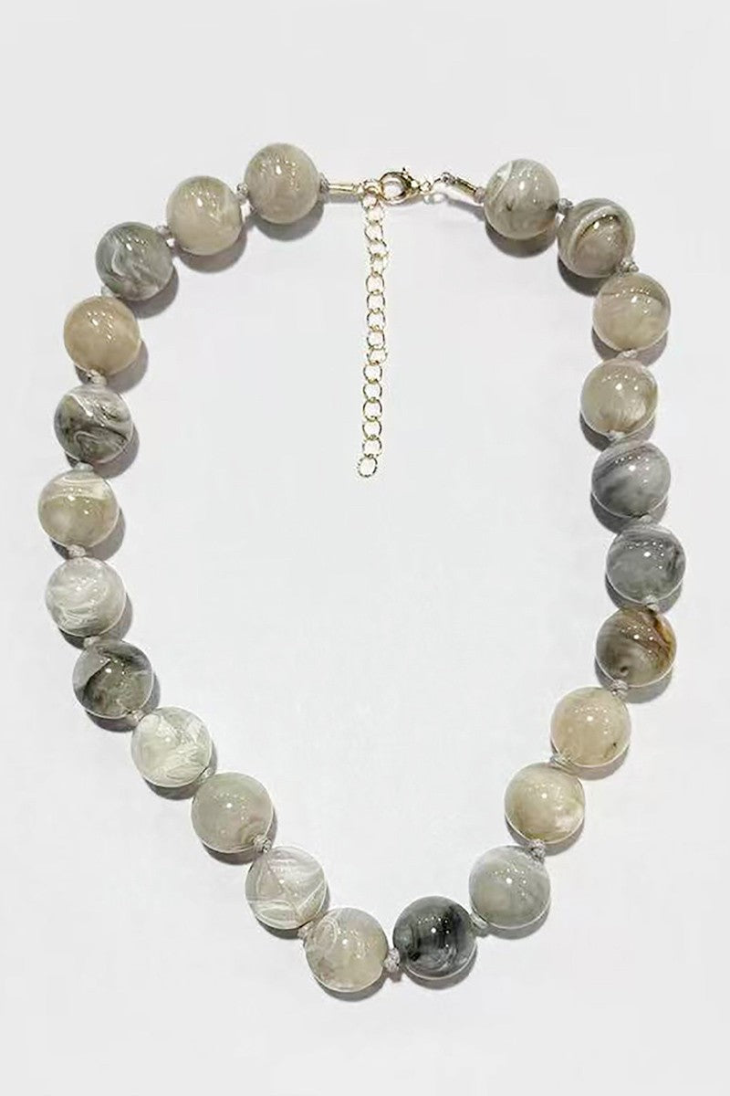 A beaded necklace made of round translucent and opaque stone beads in shades of gray, white, and beige, with a silver-tone clasp and extender chain, shown on a plain white background.