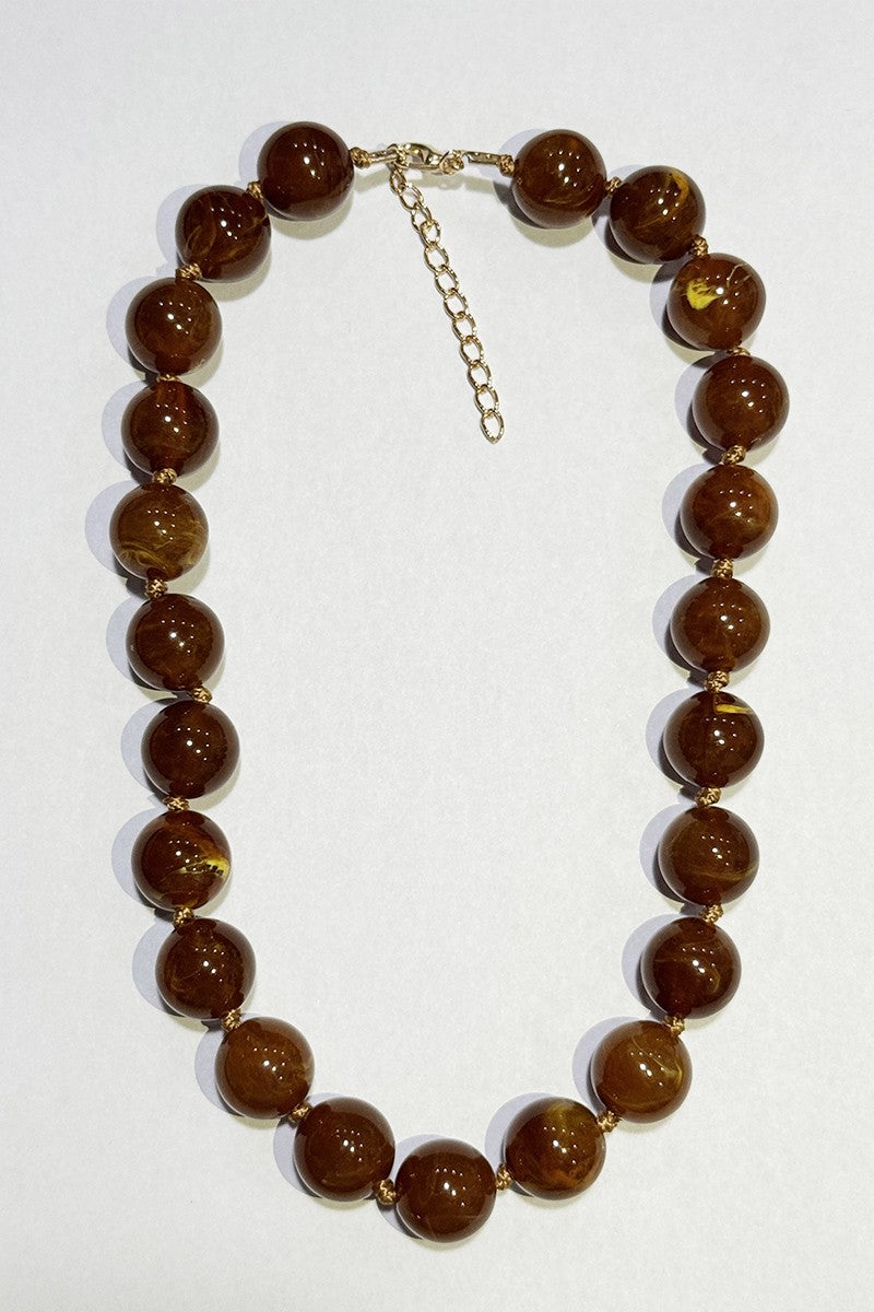 A beaded necklace made of glossy, polished brown glass beads with a gold-tone metal clasp and extender chain, displayed on a plain white background.