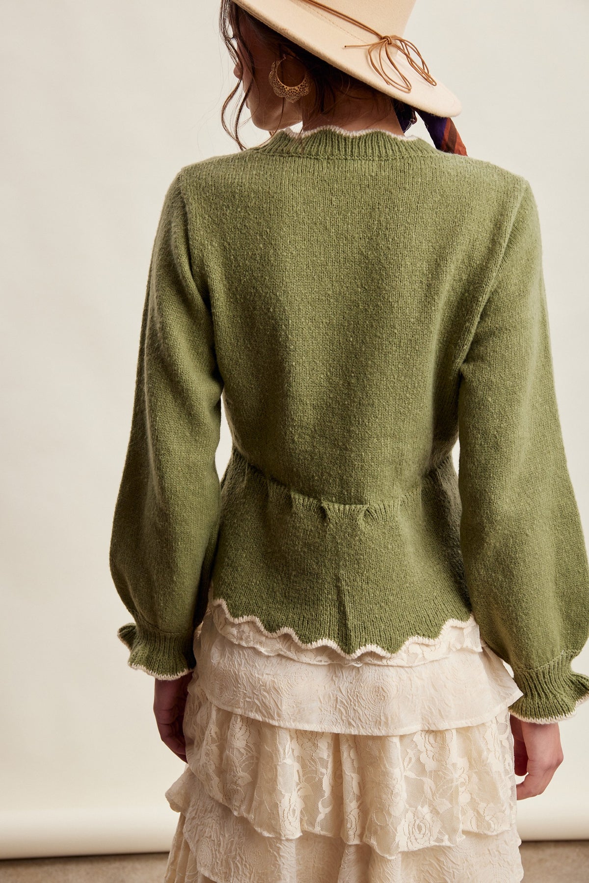 Women facing backwards wearing an olive green sweater and a hat with a lace skirt.