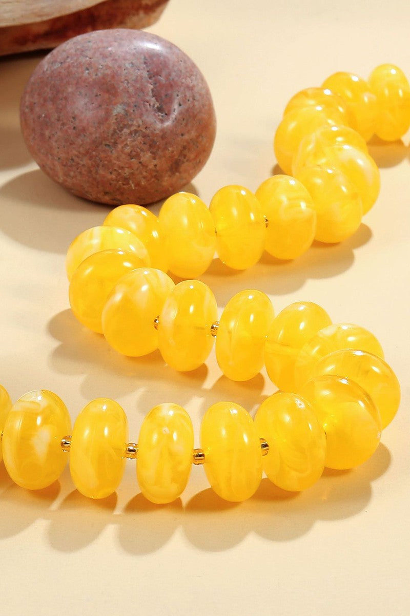 Yellow beaded bracelet on a beige surface with a stone object in the background