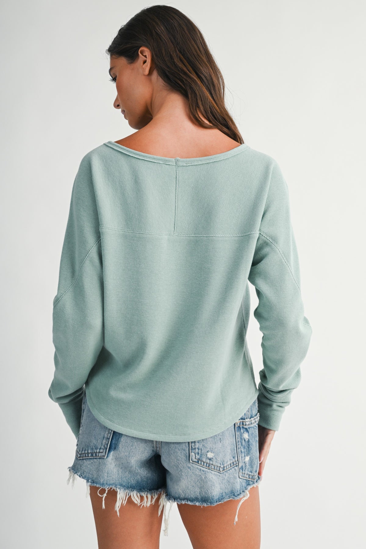 Back of a women wearing an aqua blue thermal kni long sleeve top and denim shorts.