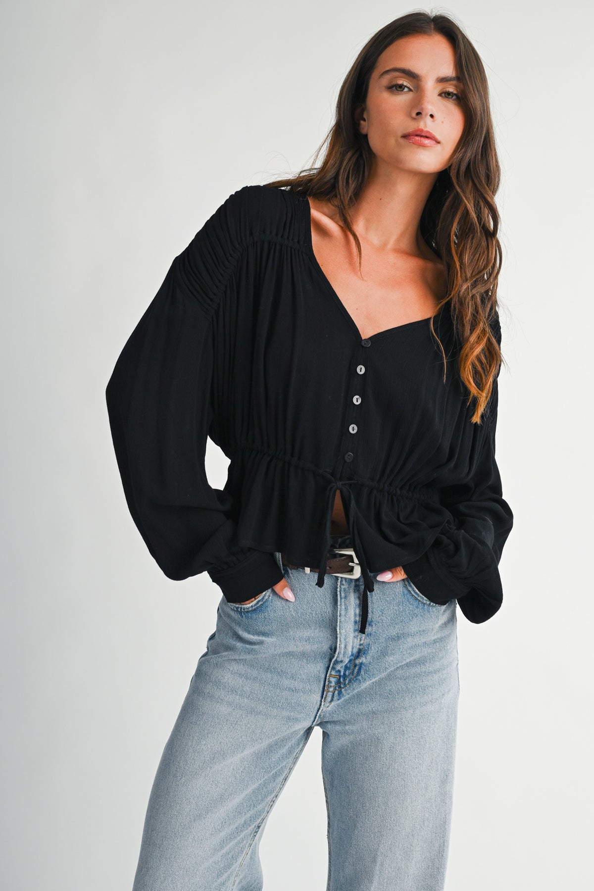 Dark haired women with textured peplum blouse in back and a pair of blue denim jeans on.