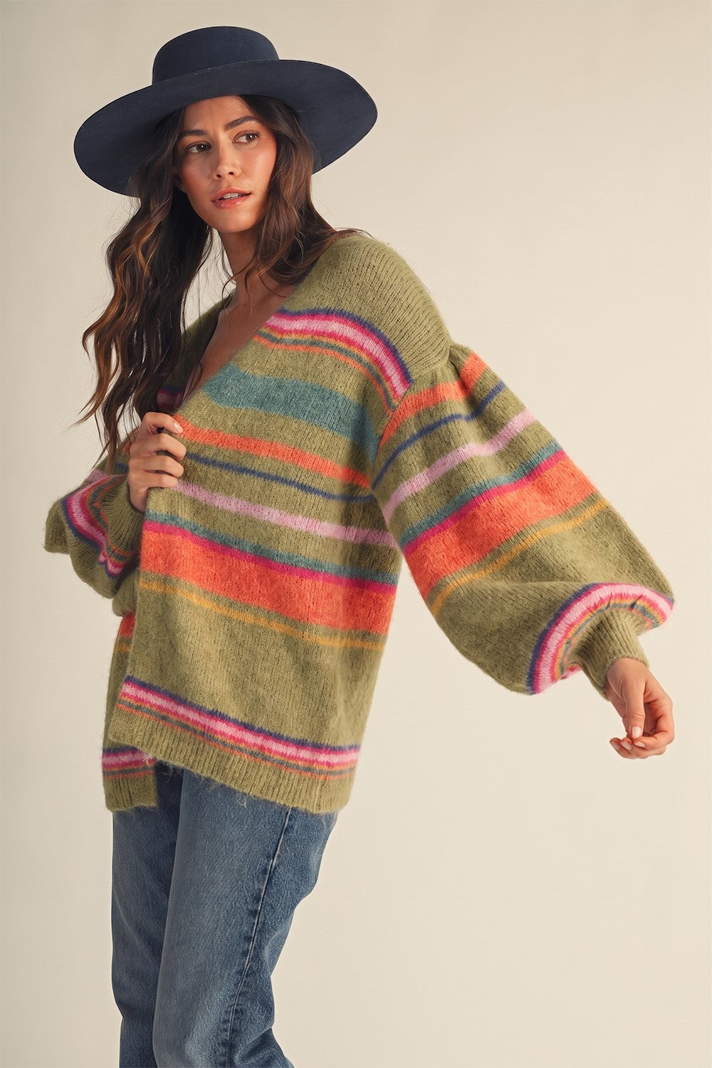 Women with multicolored stripes cardigan a blue hat and denim jeans on a plain background.