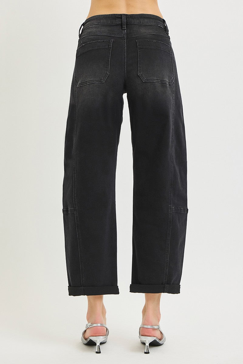 Rear view of a model wearing black cropped wide-leg barrel denim jeans with cuffed hems and silver high-heeled sandals against a light gray studio background.