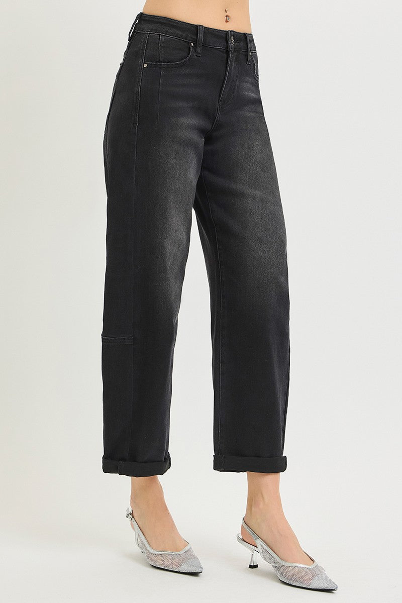 A model wearing a pair of black cropped jeans with a faded wash and cuffed hems, paired with silver pointed-toe slingback heels, against a light gray studio background.