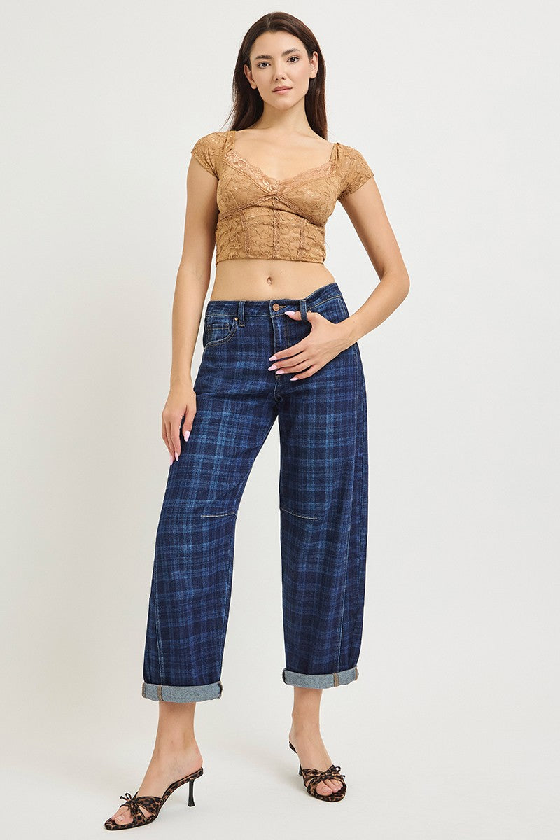 A model is wearing a tan lace crop top and dark blue plaid cropped jeans with rolled cuffs, paired with brown heeled sandals, against a plain light gray background.