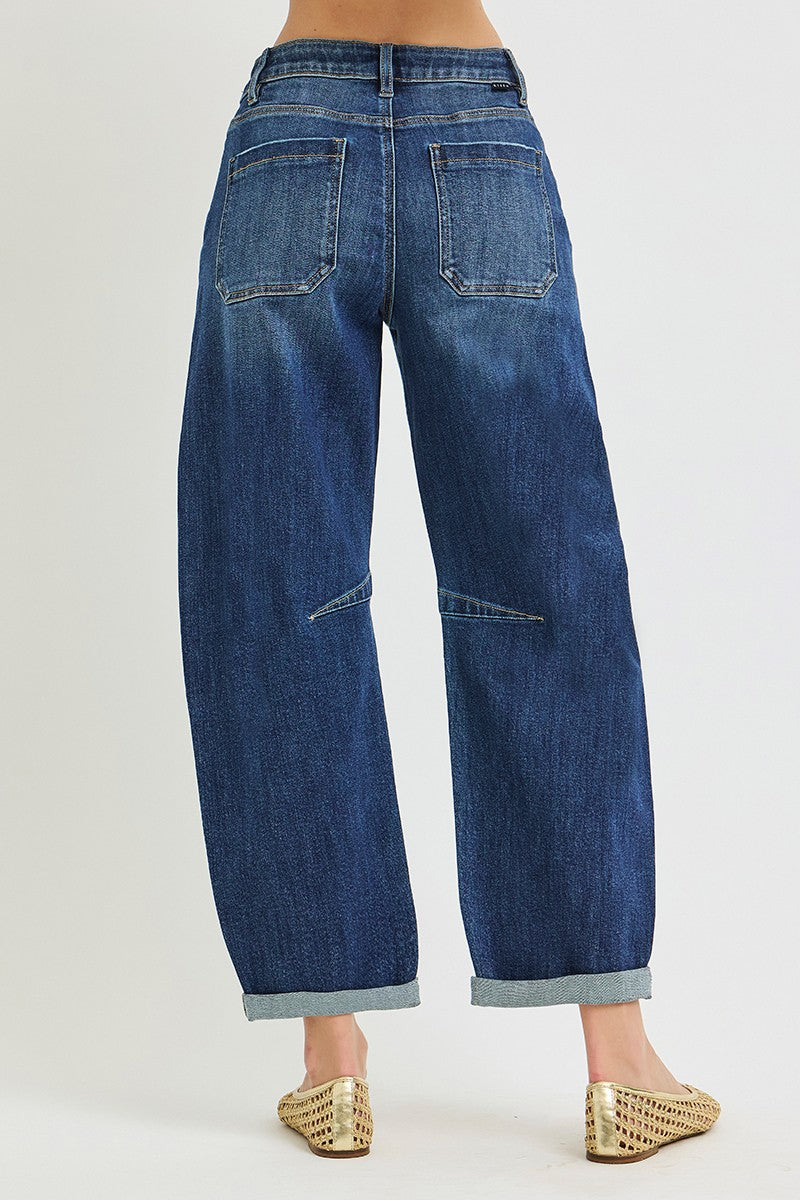 A person wearing wide-leg cropped barrel blue denim jeans with rolled cuffs and pointed woven flat shoes, shown against a plain light gray studio background.