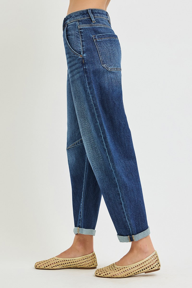 A person shown from the waist down wearing dark blue denim jeans with rolled cuffs and tan woven flat shoes against a plain light background.