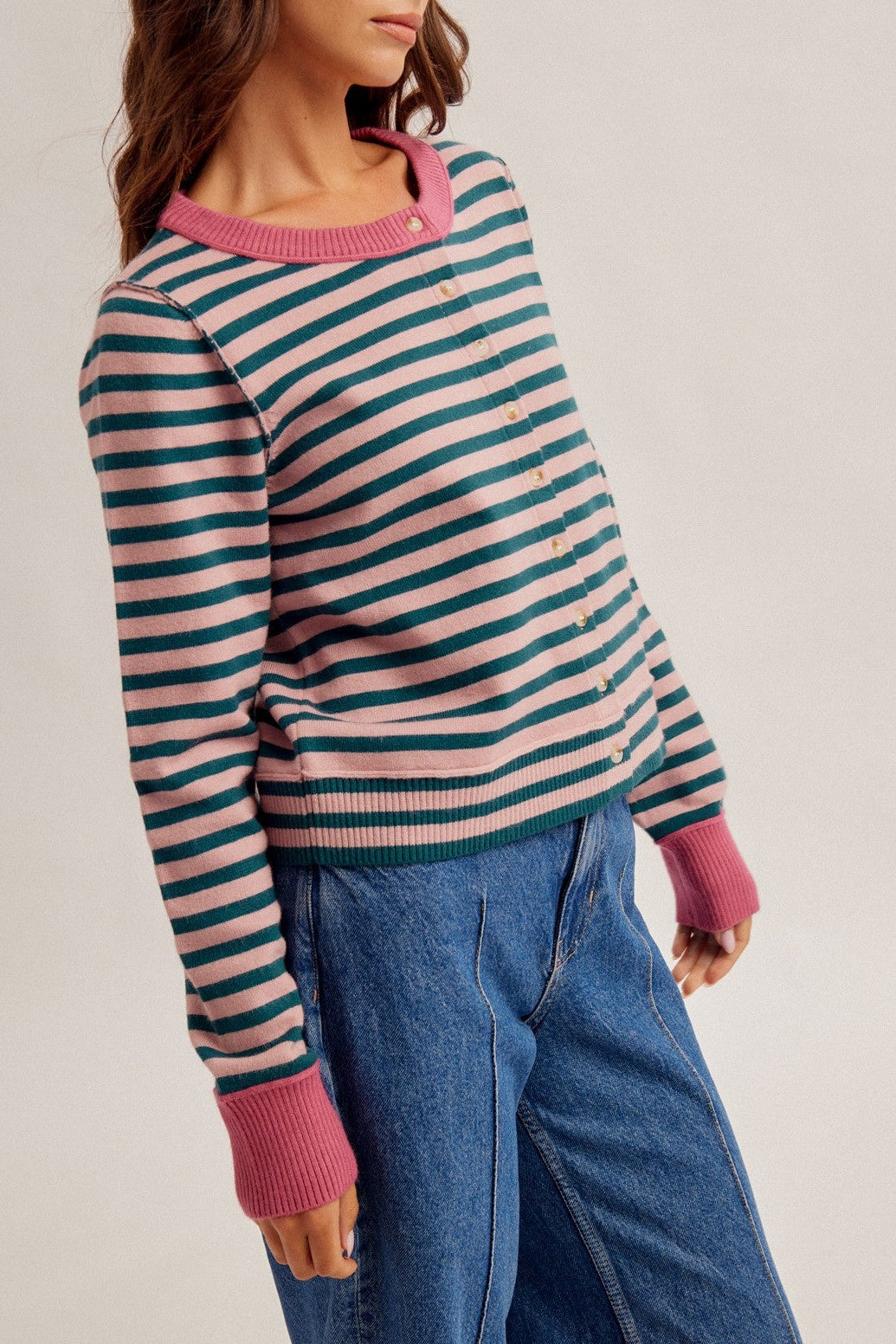 Women standing sideways wearing a stripe button down cardigan in forest green/rose and denim jeans.
