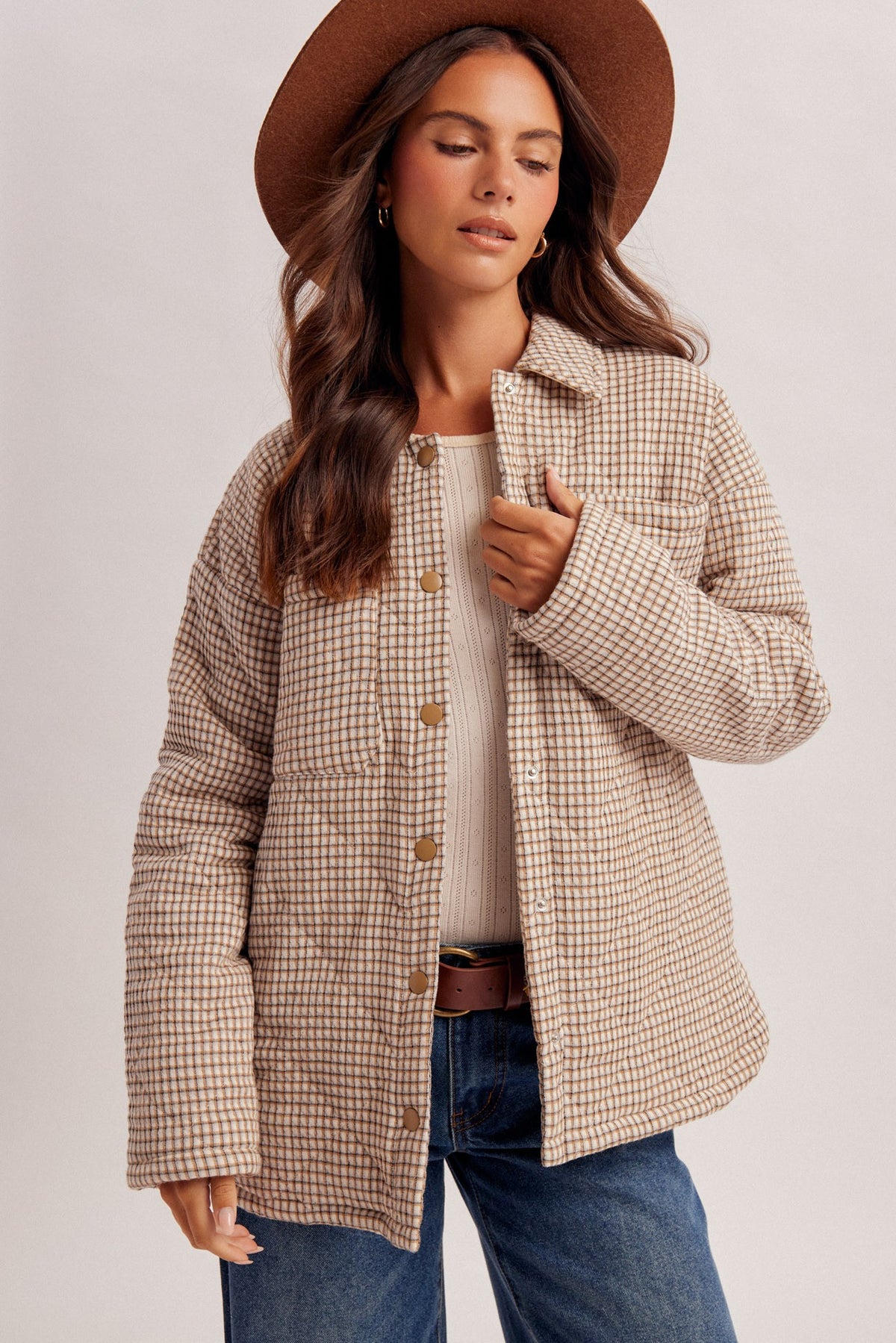 Women in a brown cowboy hat with a white shirt and a cheker oversized puffer jacket and denim blue jeans.