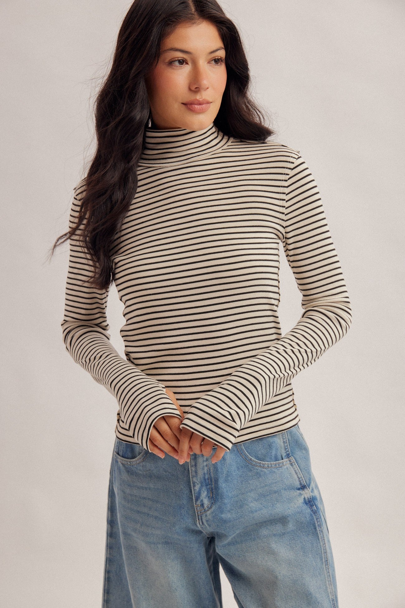 Women with dark hair wearing a stripe turtle neck in the color ecru and blue denim jeans.