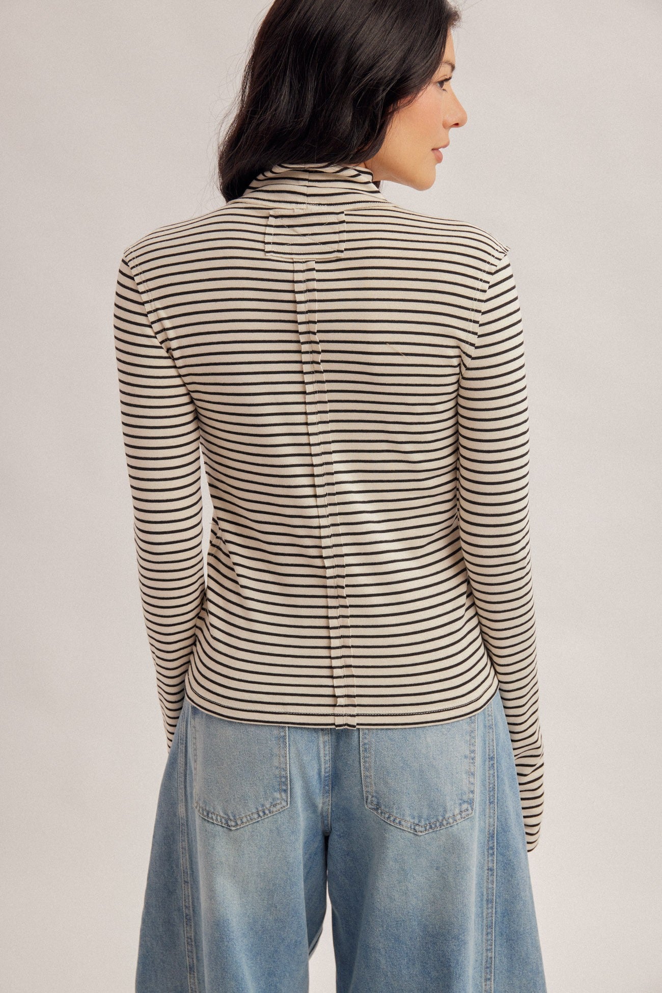 Women with dark hair wearing a stripe turtle neck in the color ecru and blue denim jeans.