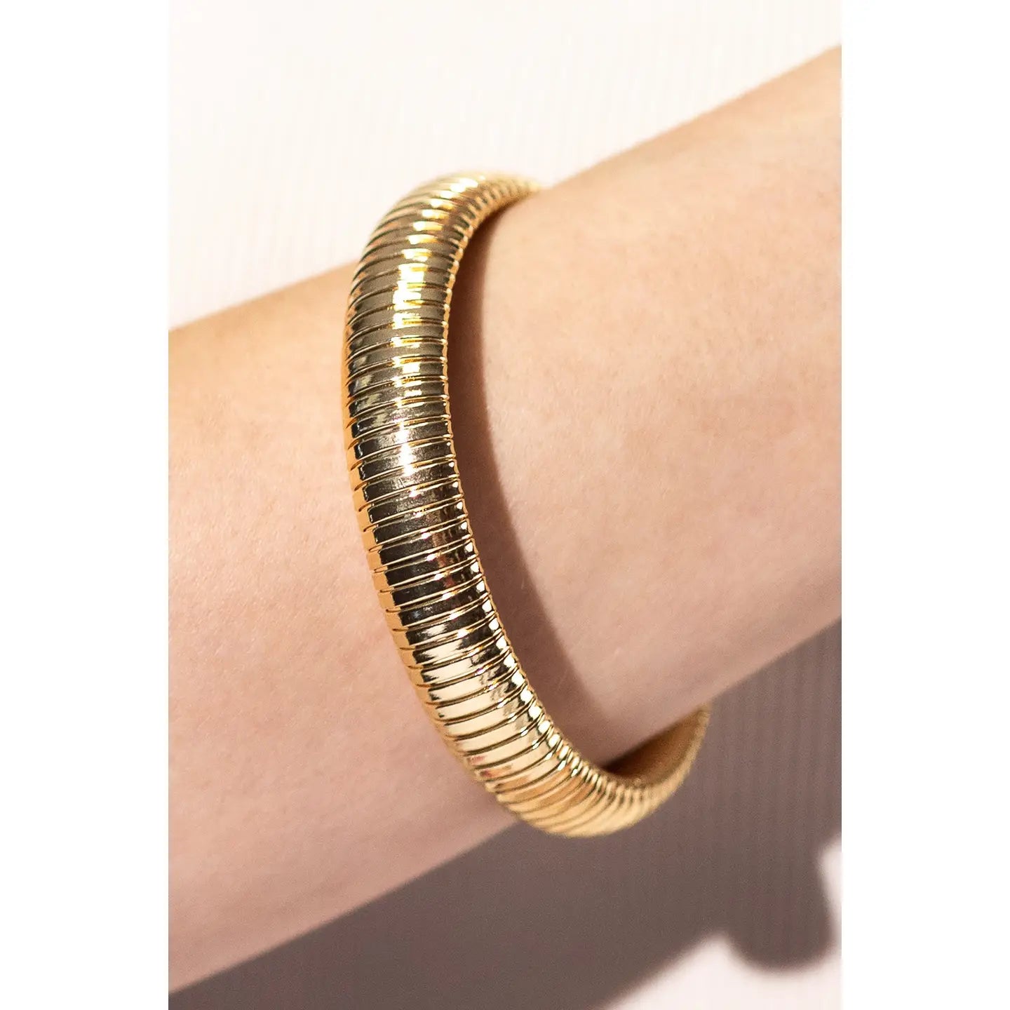 A gold-toned snake-style bangle bracelet worn on a person's wrist, shown against a light neutral background.