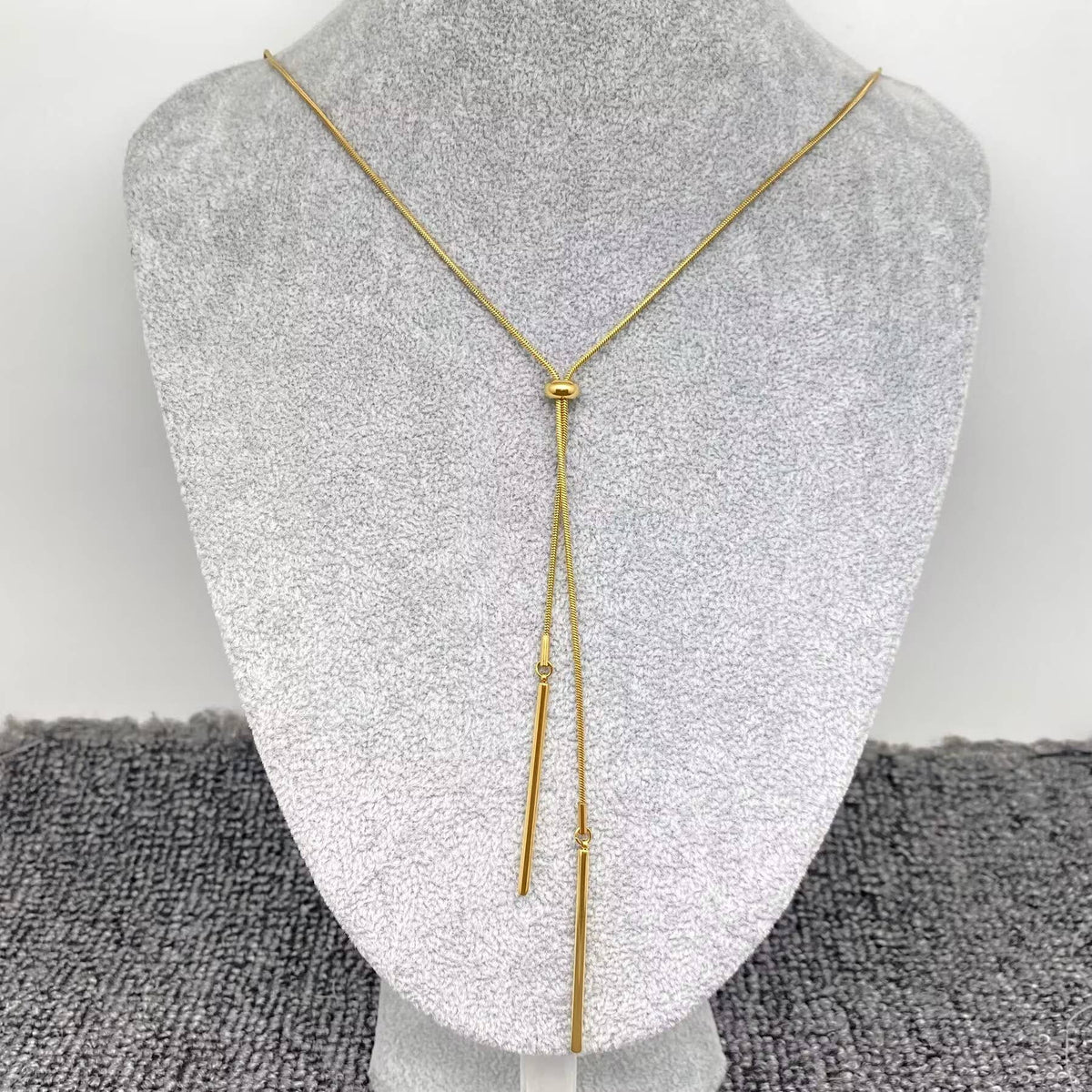 Gold  lariat necklace on a mannequin bust against a gray background