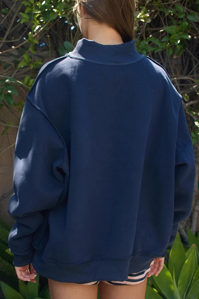 Person wearing a navy blue sweatshirt standing outdoors with greenery in the background