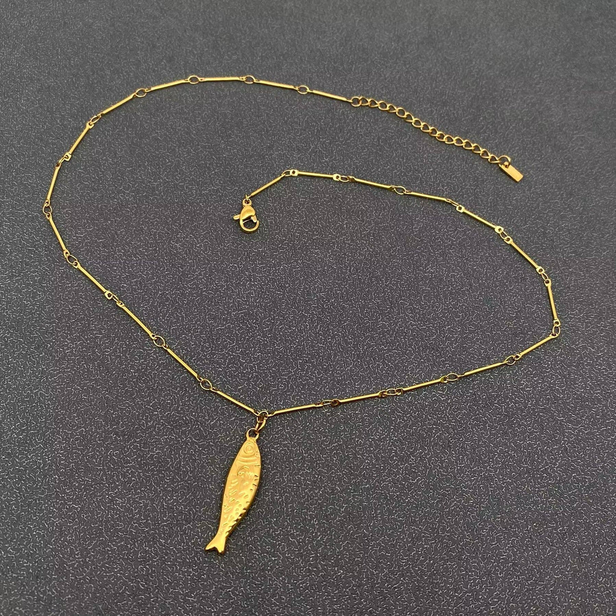 Gold necklace with a fish pendant on a gray background