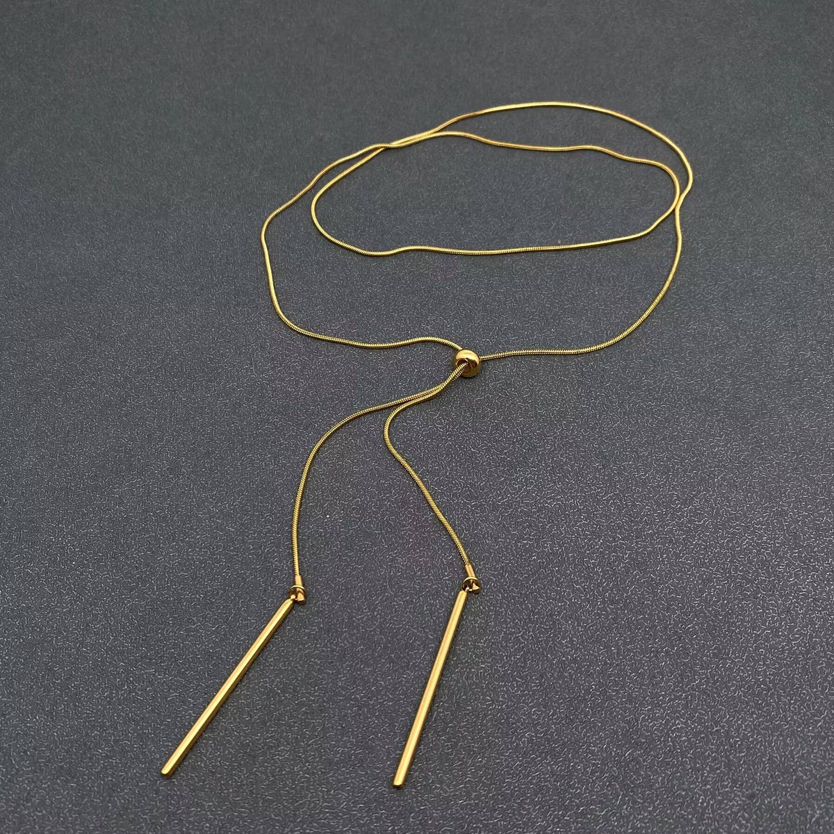 Gold  lariat necklace with two small bars on a gray background