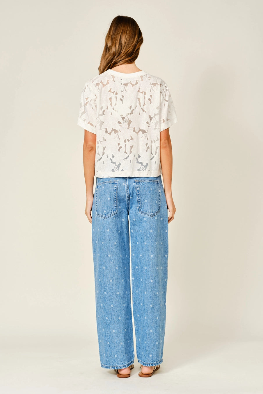 Woman wearing a white lace floral top and blue jeans on a plain background
