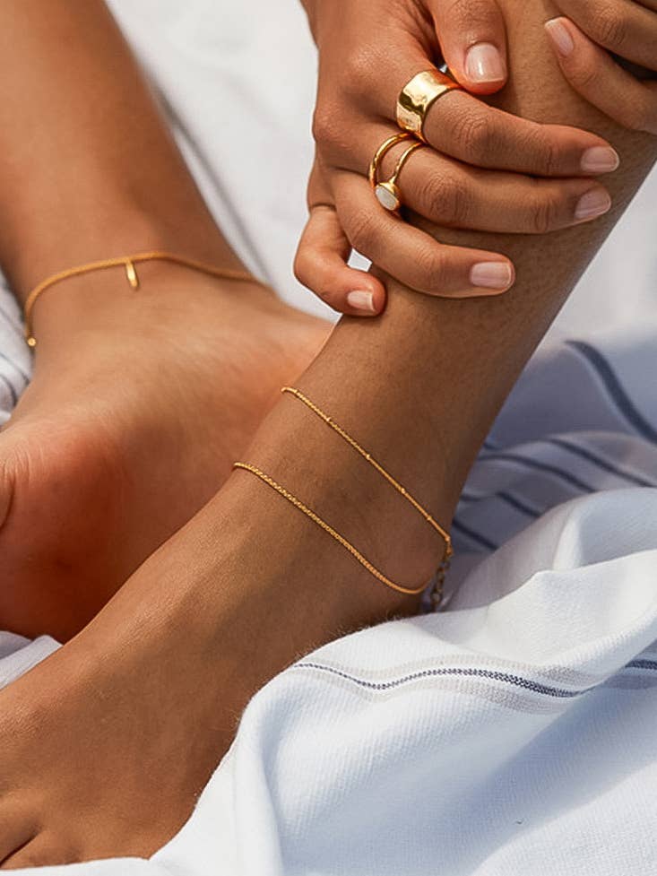 Close-up of a person's feet with gold anklets and rings on a light background