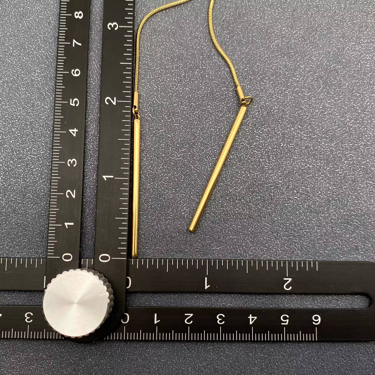 Gold lariat necklace on a gray surface with a ruler for scale