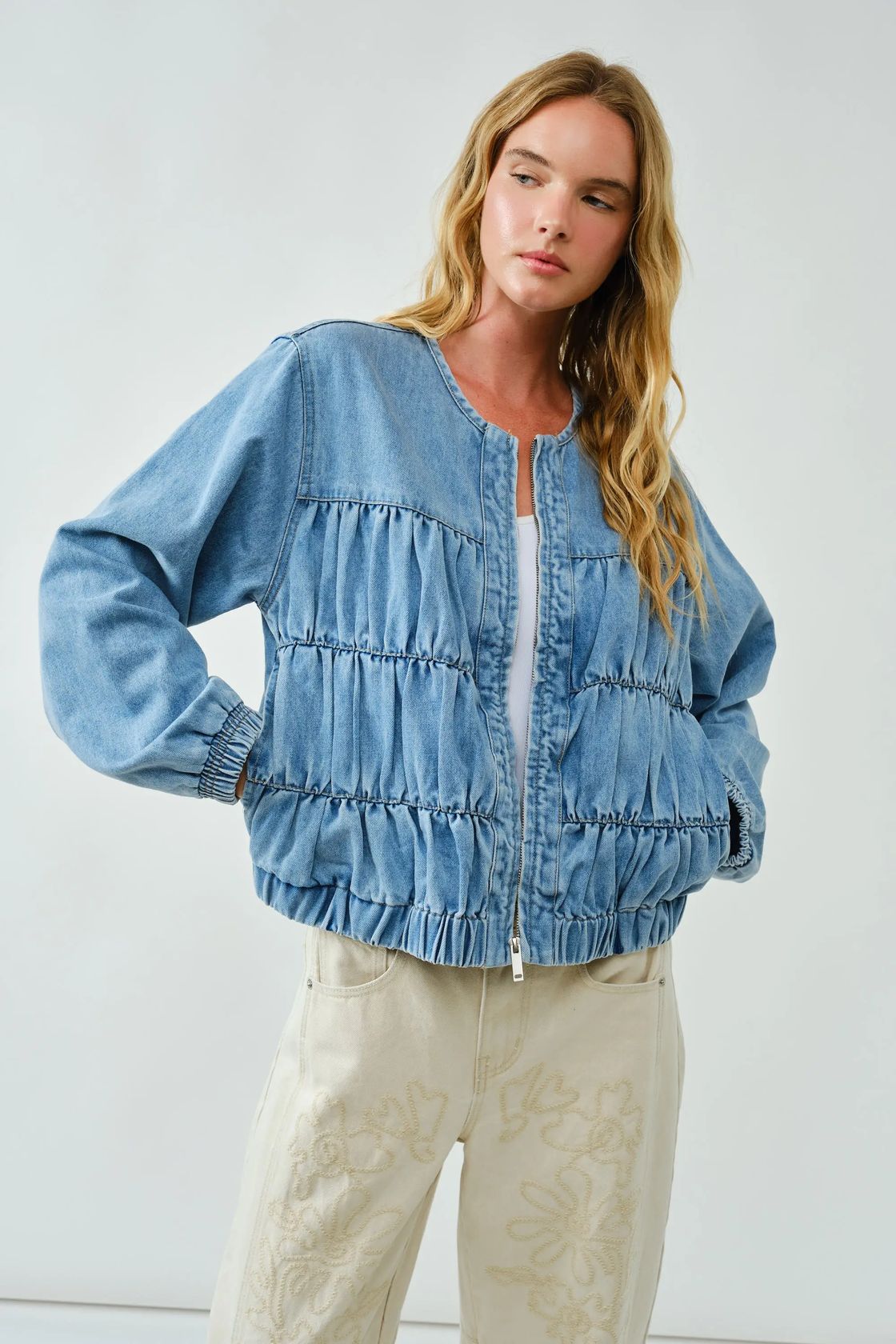 Women wearing a denim bomber jacket with light colored pants on a light gray background
