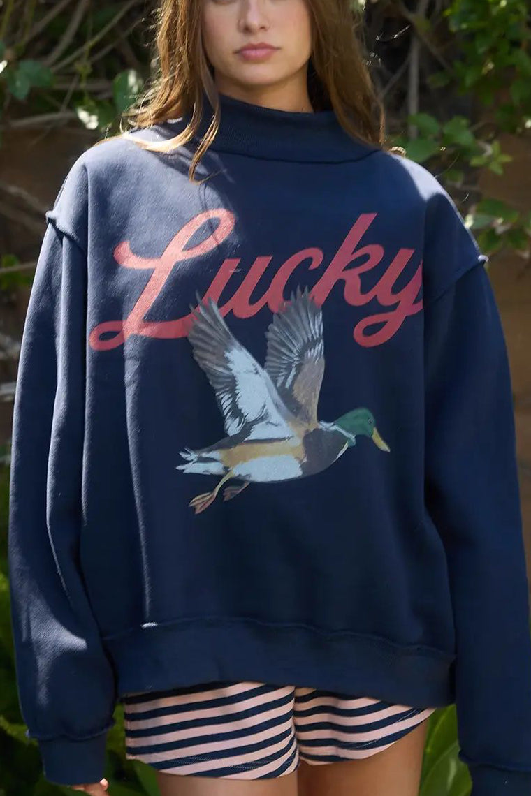 Person wearing a navy sweatshirt with 'Lucky' and a mallard duck graphic, standing outdoors.