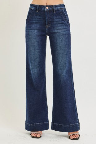 A person wearing dark blue wide-leg denim jeans with a cuffed hem and black slide sandals, shown from the waist down against a plain light background.