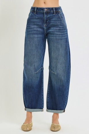 A person wearing wide-leg cropped barrel blue denim jeans with rolled cuffs and pointed woven flat shoes, shown against a plain light gray studio background.