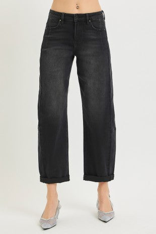 A model from the waist down wearing black wide-leg cropped barrel jeans with cuffed hems and silver pointed-toe heels, set against a plain light gray studio background.