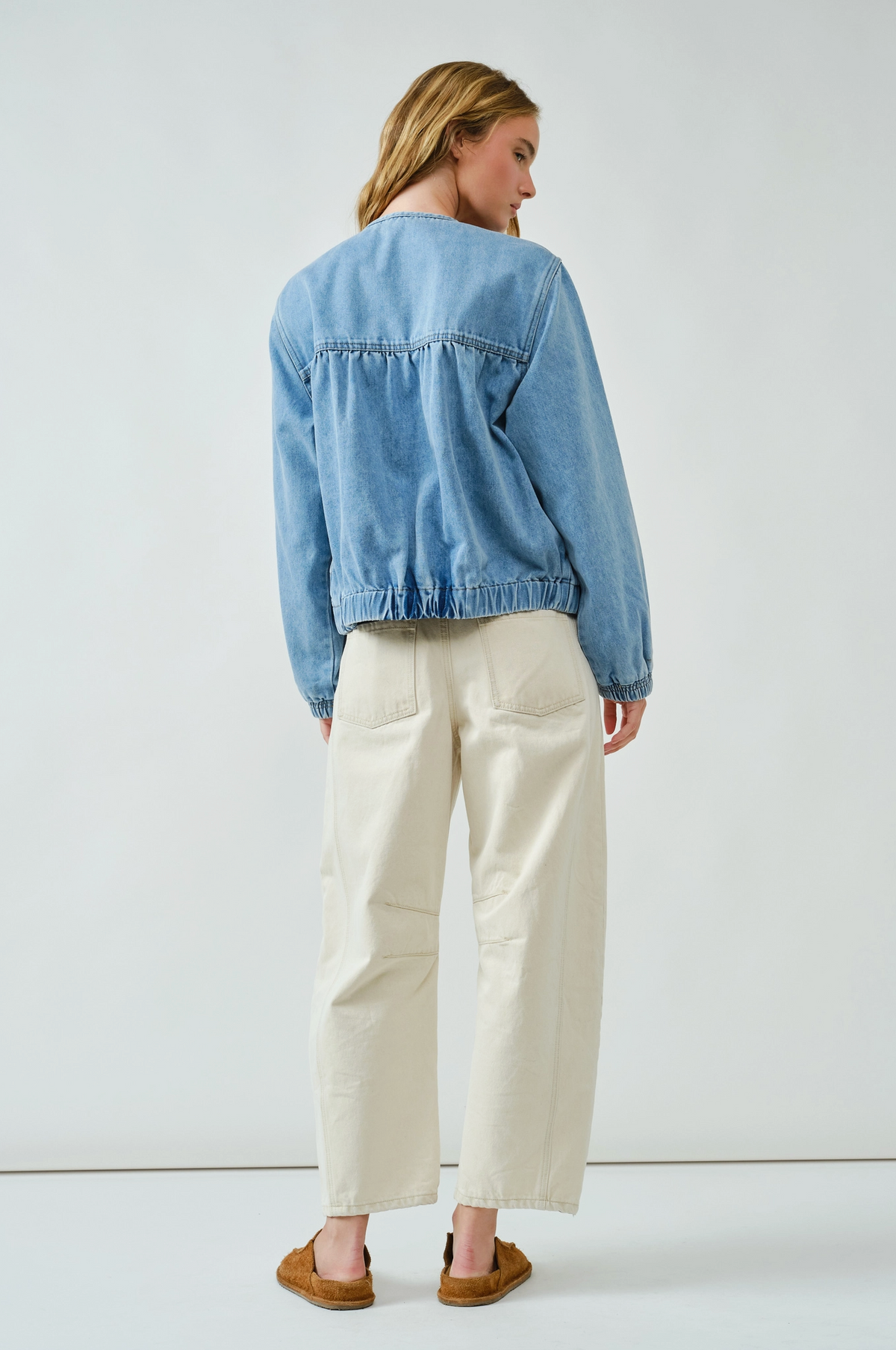 Women facing backwards with a denim jacket on and beige colored pants 