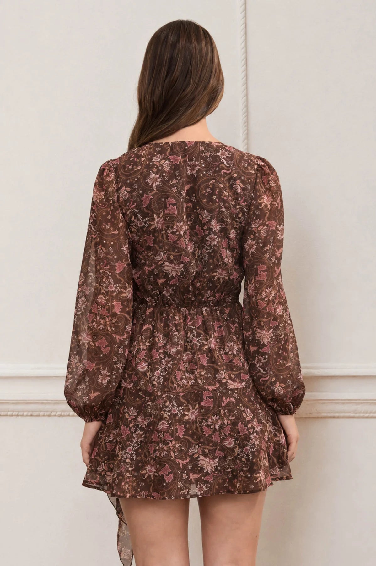Woman wearing a brown floral dress against a white wall