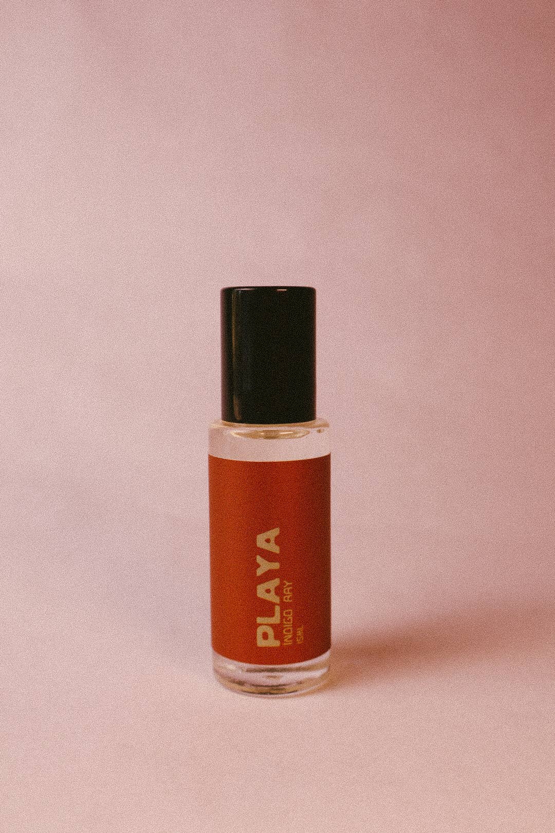 Small glass bottle with a black cap and red label with playa indigo ray on the bottle on a pink background
