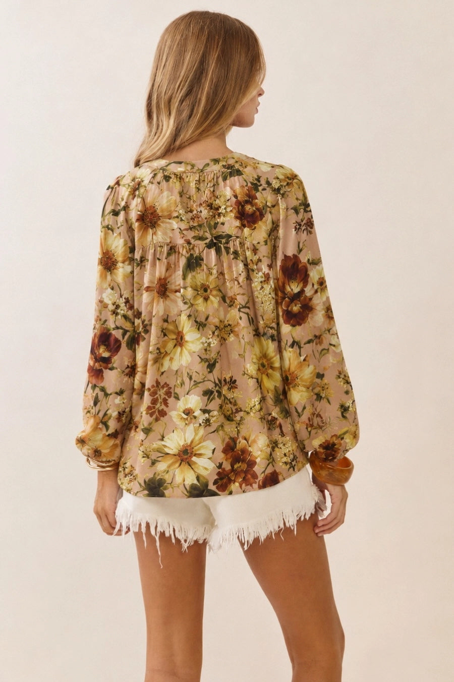 Back of a women wearing a floral print ballon sleeve blouse in a custard cream color with white shorts.