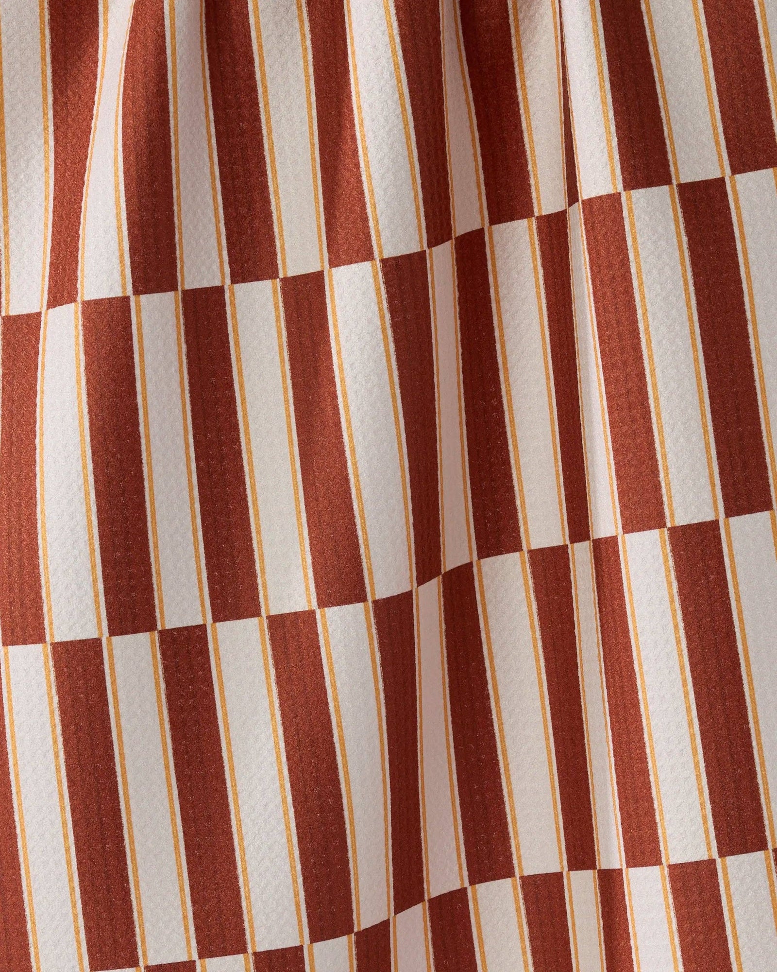 A tea towel with a rust red and cream checkerboard pattern hanging from a thin wire against a light gray studio background.