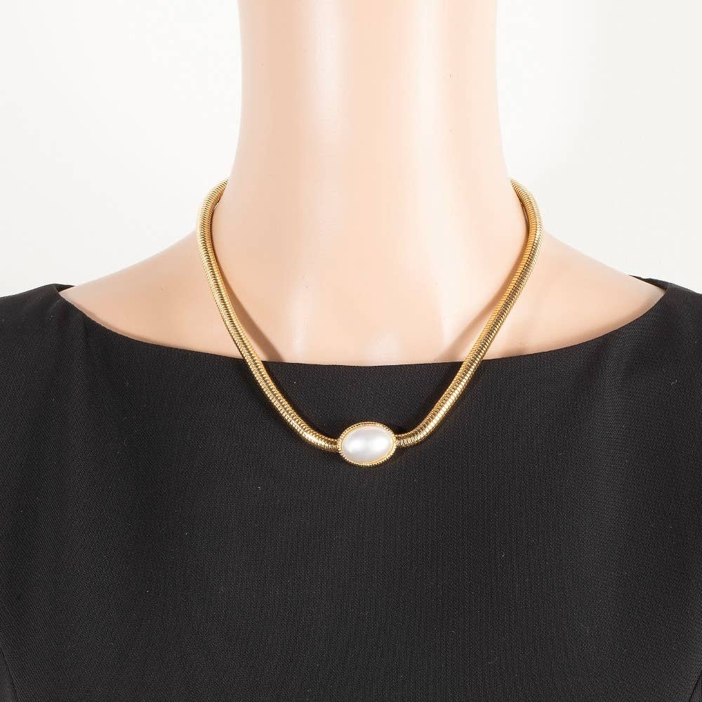 Gold necklace with a pearl pendant on a mannequin wearing a black top.