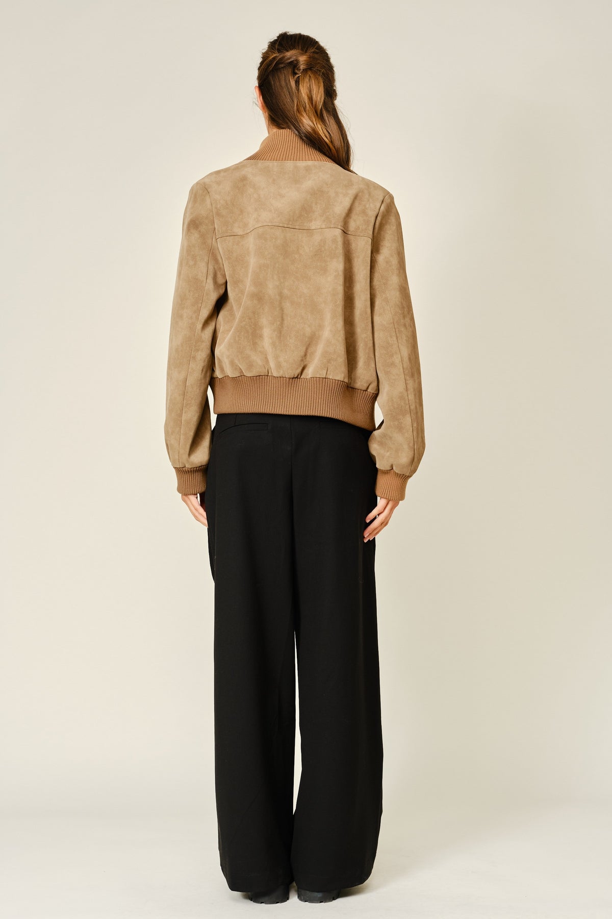 Back of a women wearing a mocha colored suede jacket and black pants.