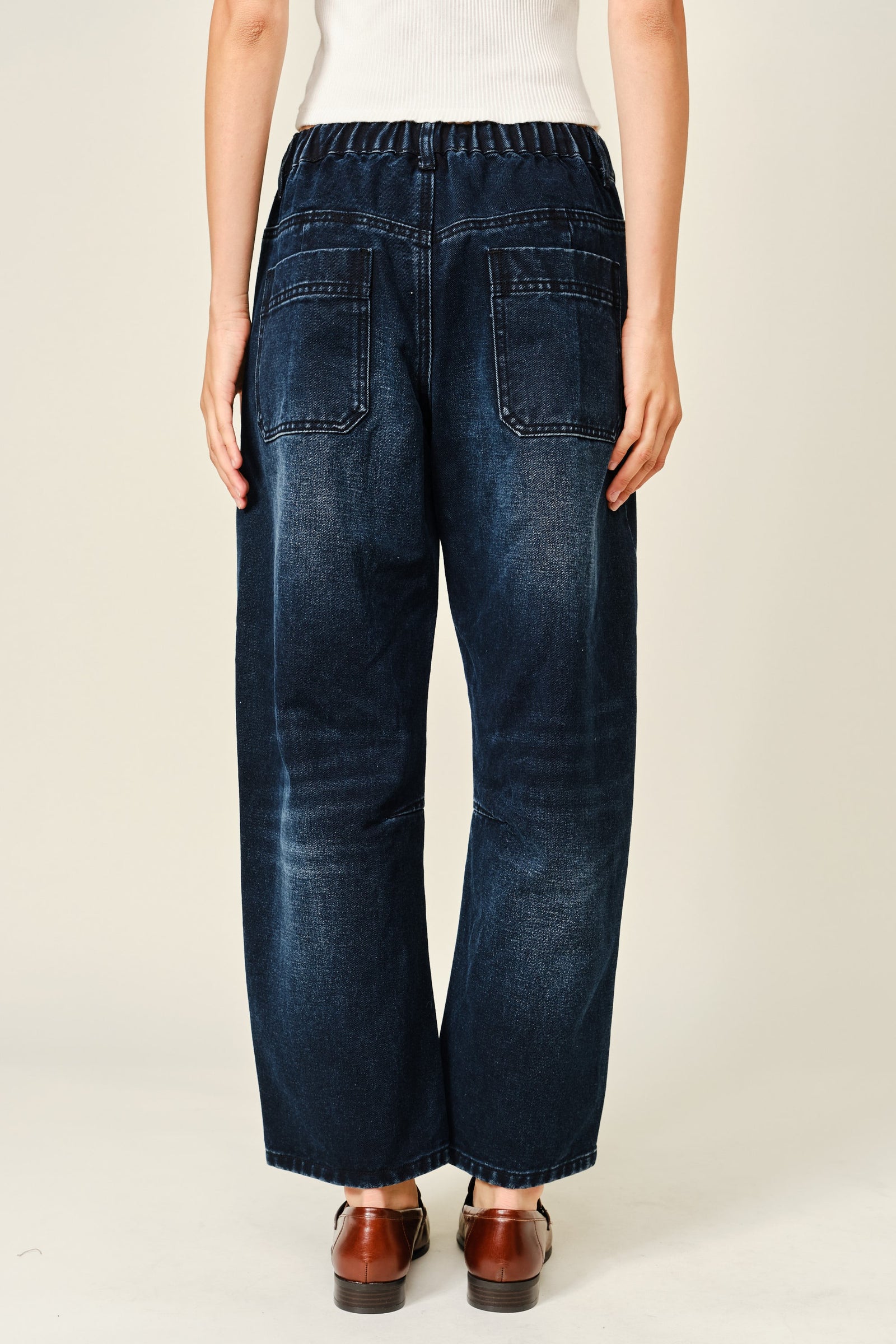 Women wearing dark washed barrel jeans and a white cropped top.