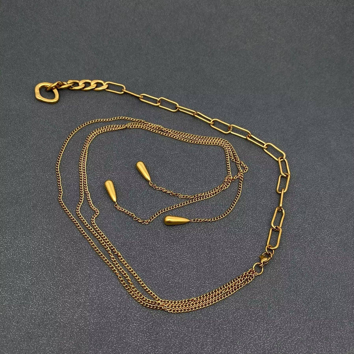 Gold chain necklace with teardrop charms on a gray background